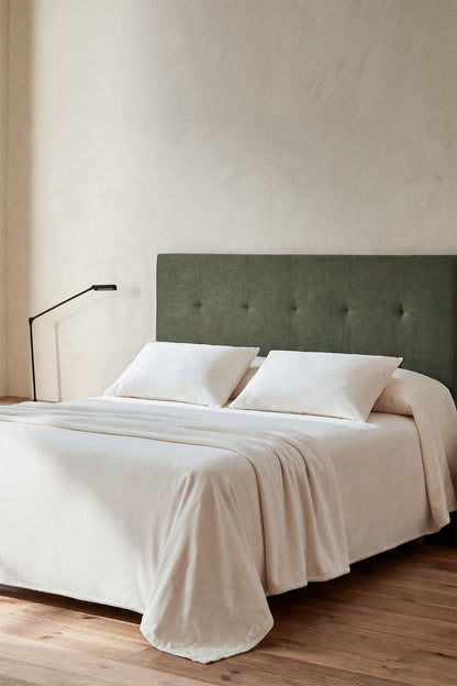 Tête de lit capitonnée sage vert installée dans une chambre